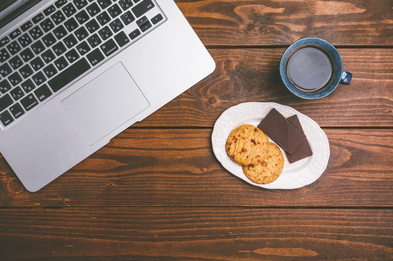 木目のデスクとノートPC、コーヒーとお菓子
